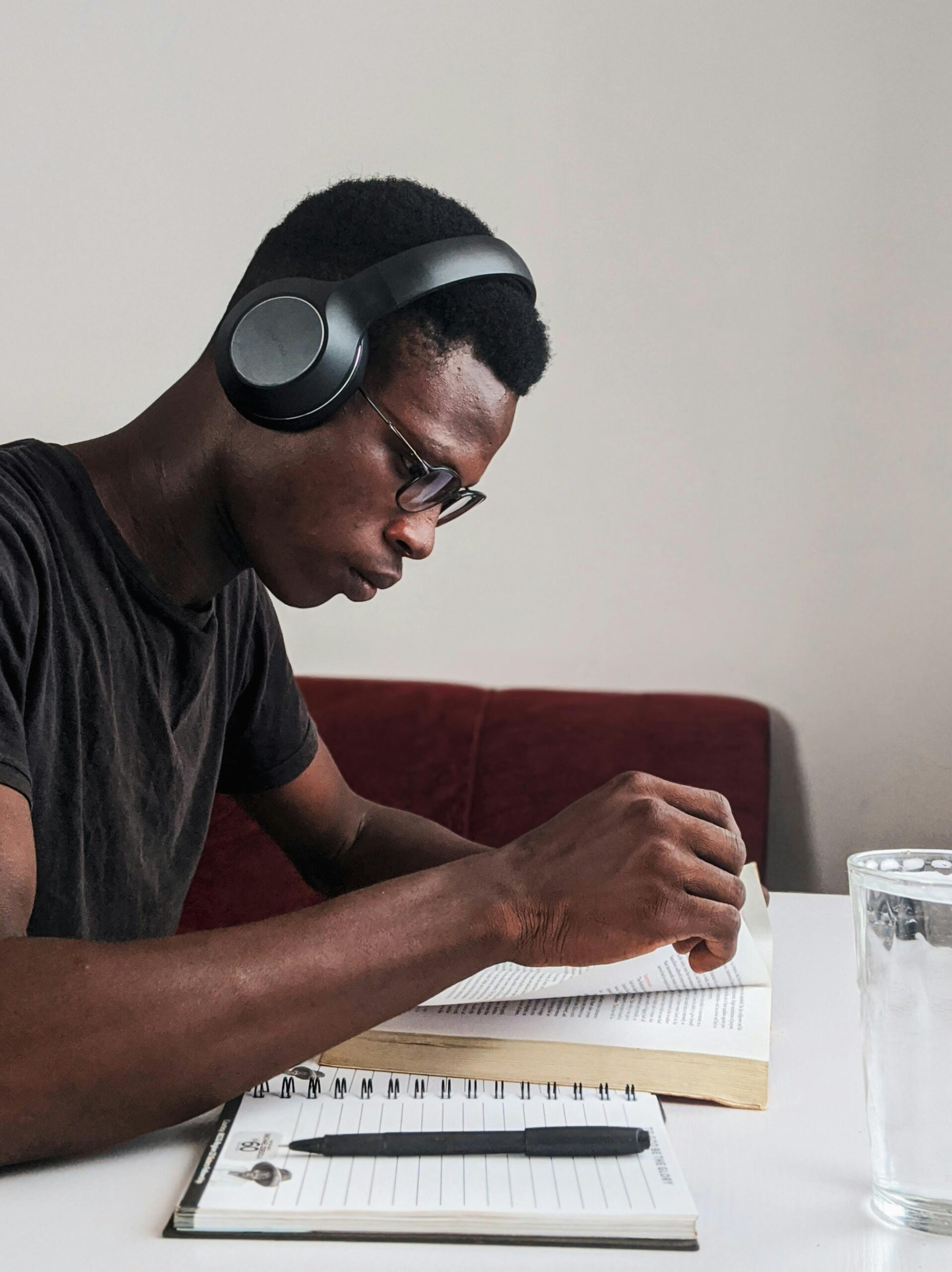 An adult man intensely studying with headphones, pen, and notebook at a desk indoors.